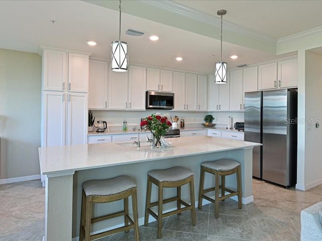 kitchen with a kitchen island with sink, hanging light fixtures, appliances with stainless steel finishes, white cabinetry, and a breakfast bar area