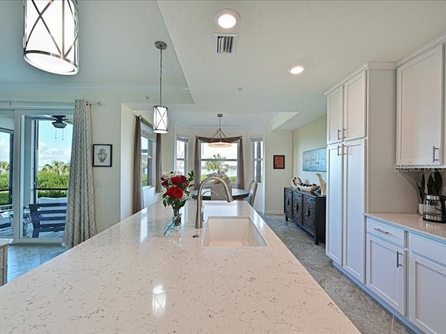 kitchen with pendant lighting, light stone counters, white cabinetry, and sink