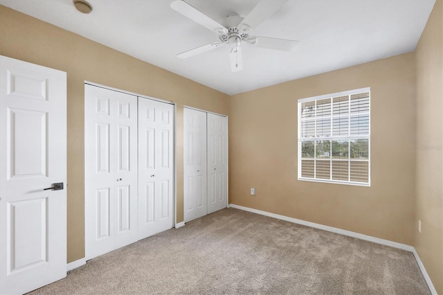 unfurnished bedroom featuring ceiling fan, light carpet, and two closets