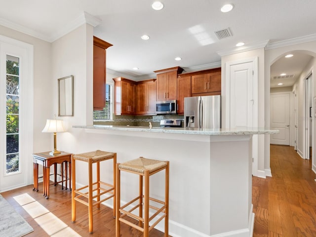 kitchen with kitchen peninsula, appliances with stainless steel finishes, light hardwood / wood-style floors, and ornamental molding