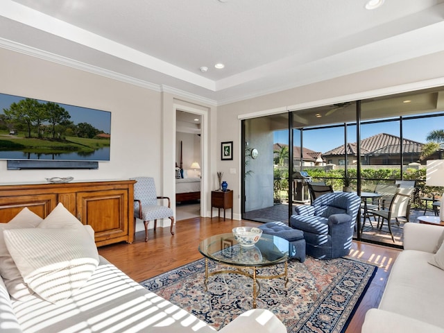 living room with hardwood / wood-style flooring, a tray ceiling, and ornamental molding