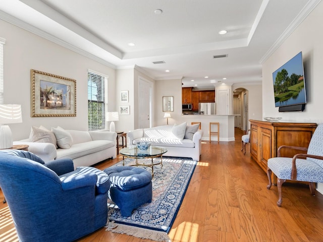 living room featuring light hardwood / wood-style floors, a raised ceiling, and ornamental molding