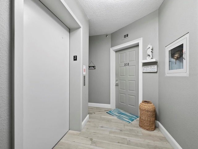 doorway to outside with a textured ceiling, elevator, and light hardwood / wood-style floors