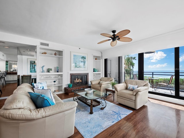 living room with built in shelves, ceiling fan, hardwood / wood-style floors, and a fireplace