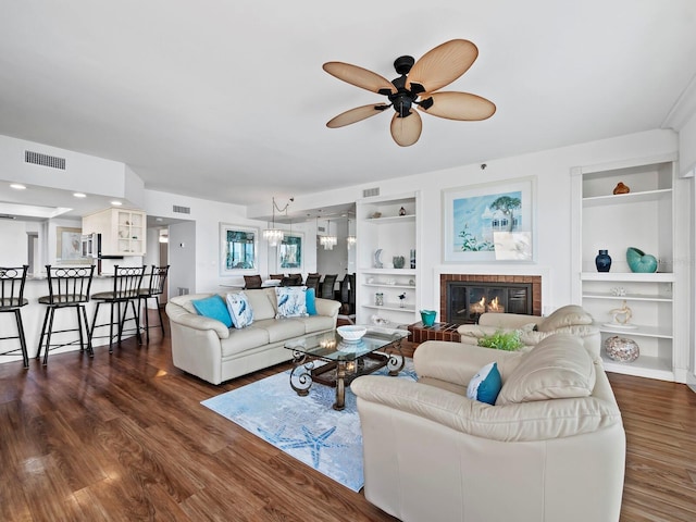 living room with a fireplace, built in shelves, dark hardwood / wood-style flooring, and ceiling fan