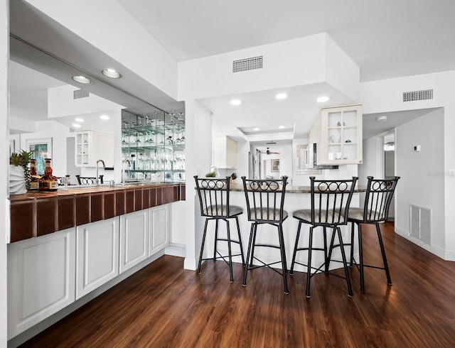 kitchen with kitchen peninsula, a kitchen breakfast bar, dark hardwood / wood-style flooring, and white cabinetry