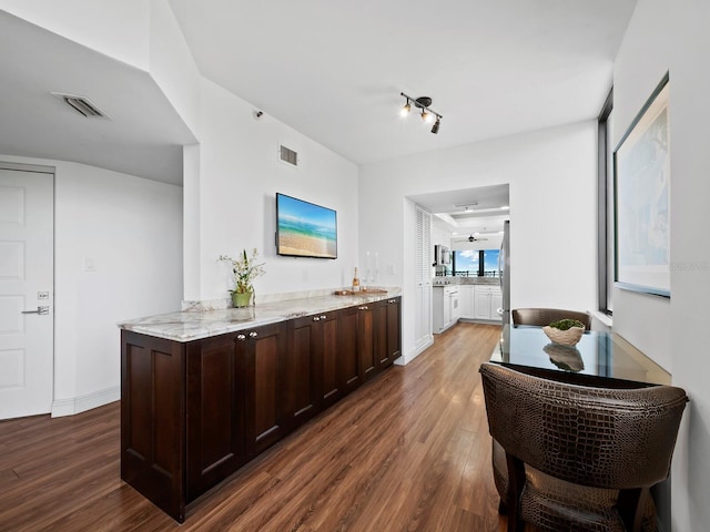 bar featuring light stone counters, dark brown cabinets, and dark hardwood / wood-style floors