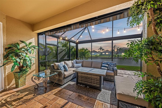 patio terrace at dusk with outdoor lounge area, a water view, and a lanai