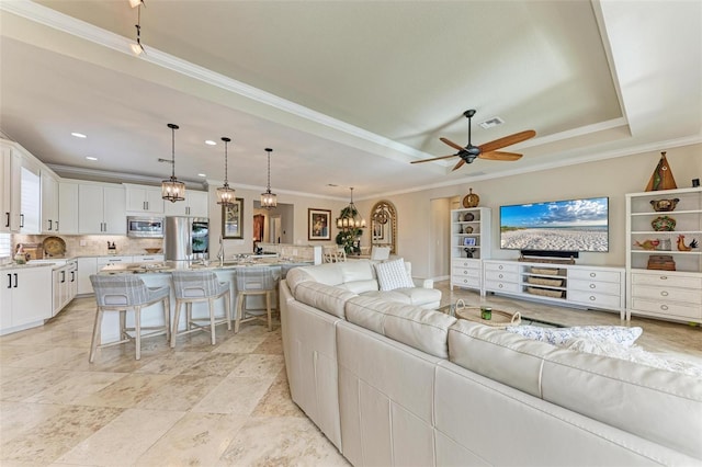 living room featuring ceiling fan with notable chandelier, a raised ceiling, and crown molding