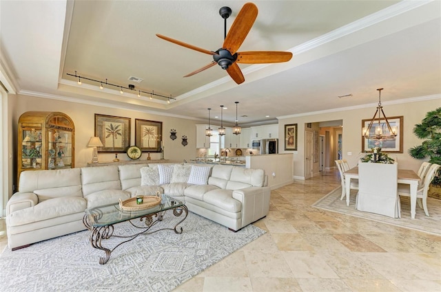 living room with ceiling fan with notable chandelier, track lighting, a raised ceiling, and ornamental molding