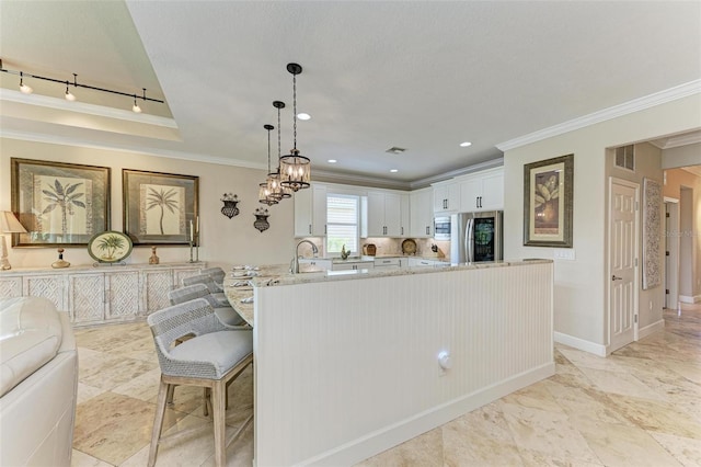 kitchen with light stone counters, ornamental molding, decorative light fixtures, white cabinetry, and stainless steel refrigerator