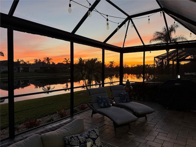 patio terrace at dusk with a lanai, a water view, and grilling area