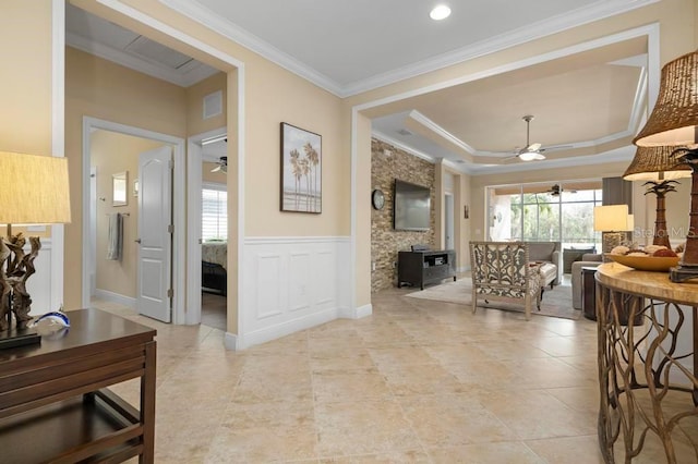 interior space with a raised ceiling, ceiling fan, and crown molding