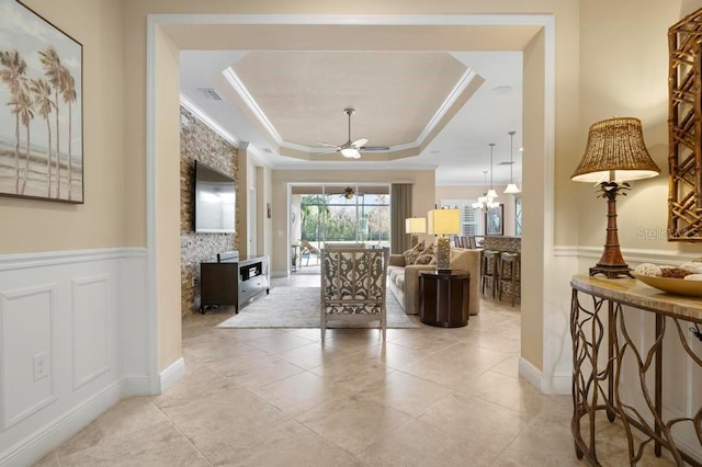 interior space with ceiling fan with notable chandelier, a raised ceiling, and crown molding