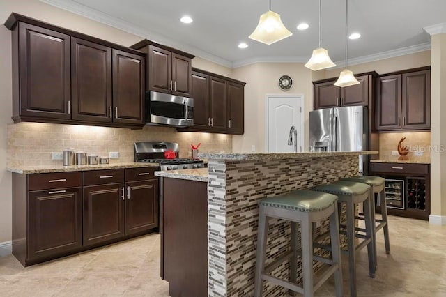 kitchen with appliances with stainless steel finishes, a kitchen breakfast bar, crown molding, hanging light fixtures, and an island with sink