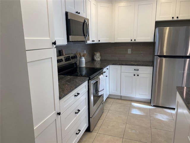 kitchen featuring white cabinetry, stainless steel appliances, backsplash, dark stone countertops, and light tile patterned floors