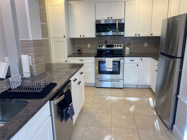 kitchen with white cabinetry, stainless steel appliances, dark stone counters, and tasteful backsplash