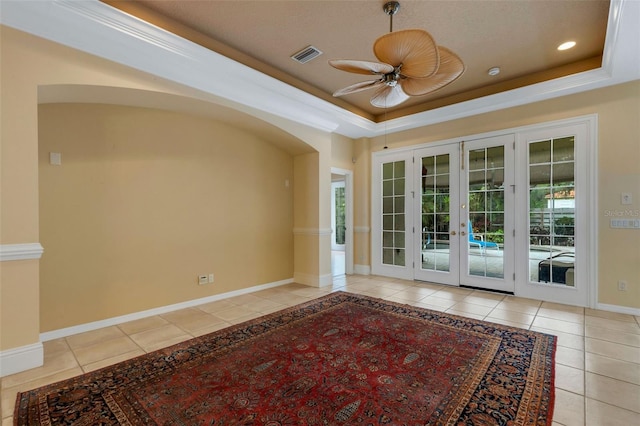 tiled empty room featuring french doors, a tray ceiling, ceiling fan, and crown molding