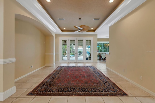 entrance foyer with french doors, a raised ceiling, crown molding, ceiling fan, and light tile patterned floors