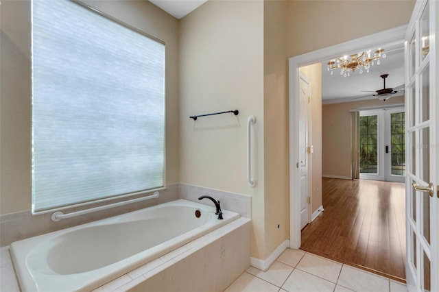 bathroom with tile patterned flooring, french doors, ceiling fan with notable chandelier, and tiled bath