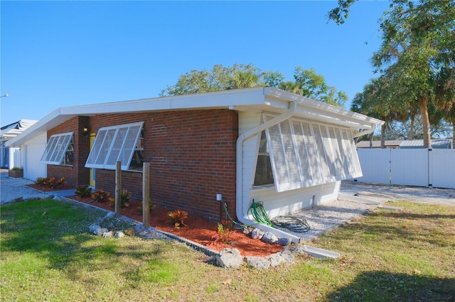 view of side of home with brick siding, a lawn, and fence