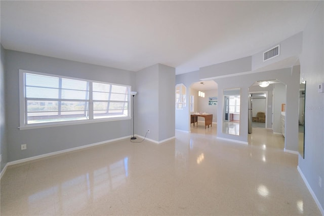 spare room featuring plenty of natural light, baseboards, visible vents, and arched walkways