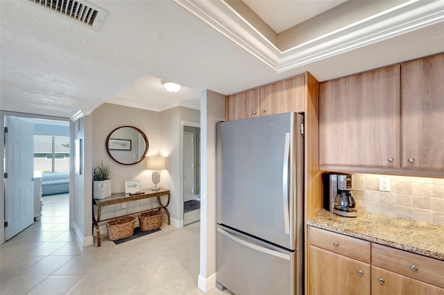 kitchen featuring decorative backsplash, light stone counters, crown molding, light tile patterned floors, and stainless steel refrigerator