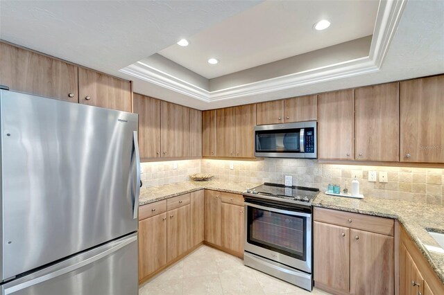 kitchen with light stone countertops, stainless steel appliances, tasteful backsplash, a tray ceiling, and light tile patterned floors