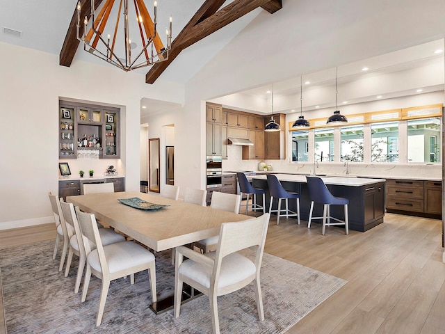 dining room with an inviting chandelier, lofted ceiling with beams, and light wood-type flooring