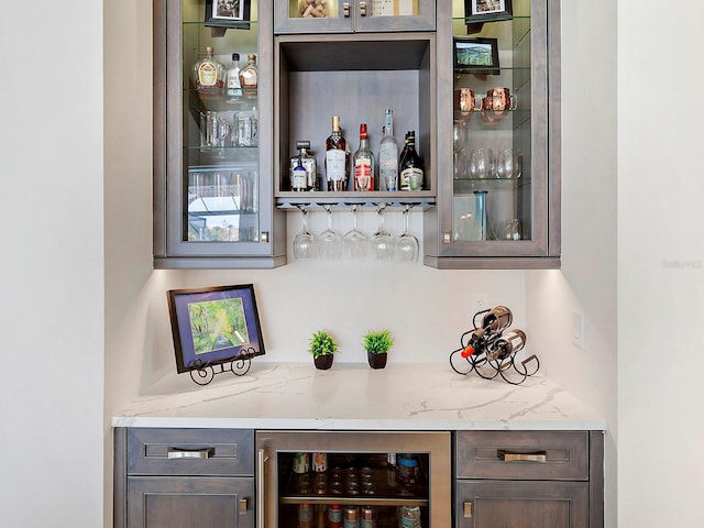 bar with wine cooler, light stone countertops, and dark brown cabinets