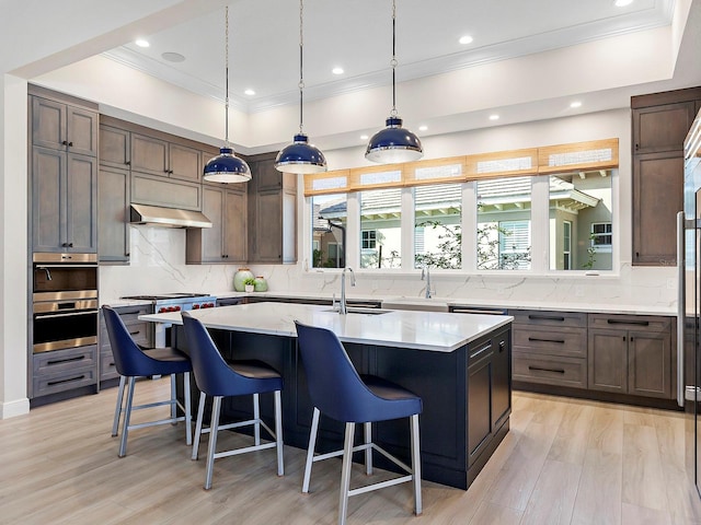 kitchen featuring a kitchen breakfast bar, extractor fan, a kitchen island with sink, sink, and pendant lighting