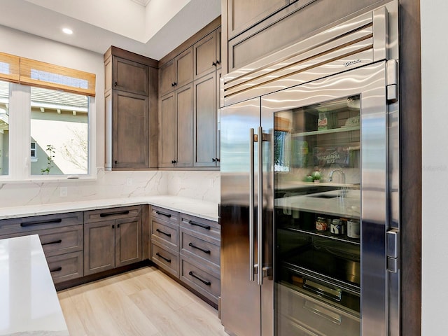 kitchen featuring light hardwood / wood-style flooring, dark brown cabinetry, tasteful backsplash, light stone counters, and stainless steel built in refrigerator