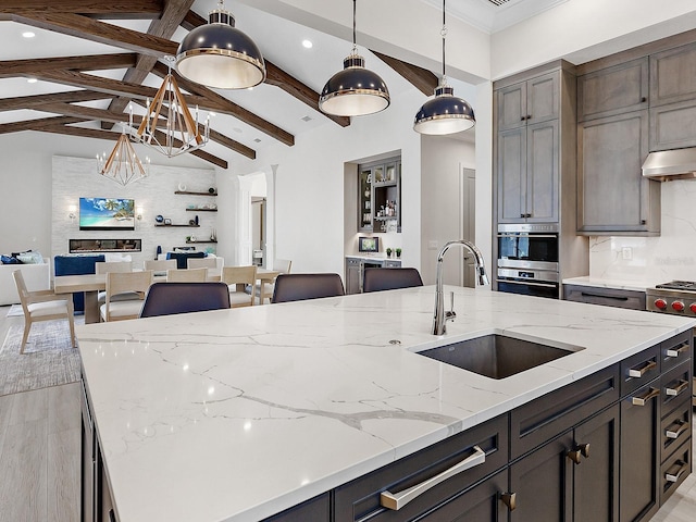 kitchen featuring light stone countertops, vaulted ceiling with beams, hanging light fixtures, and sink