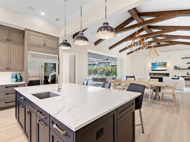 kitchen with a large island with sink, sink, built in refrigerator, vaulted ceiling with beams, and decorative light fixtures