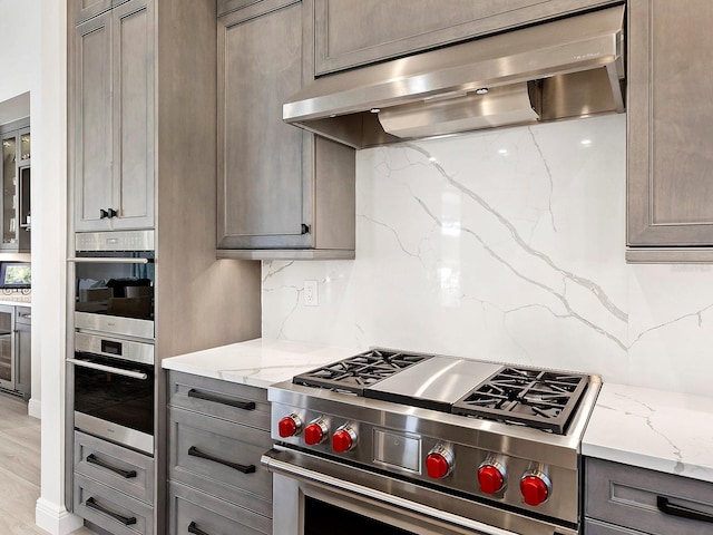 kitchen with decorative backsplash, light stone counters, high end stainless steel range oven, and exhaust hood