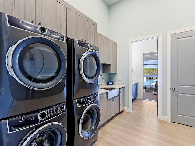 clothes washing area with cabinets, light hardwood / wood-style flooring, stacked washer / drying machine, and sink