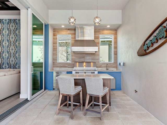 kitchen with a breakfast bar, a center island, hanging light fixtures, and wall chimney exhaust hood