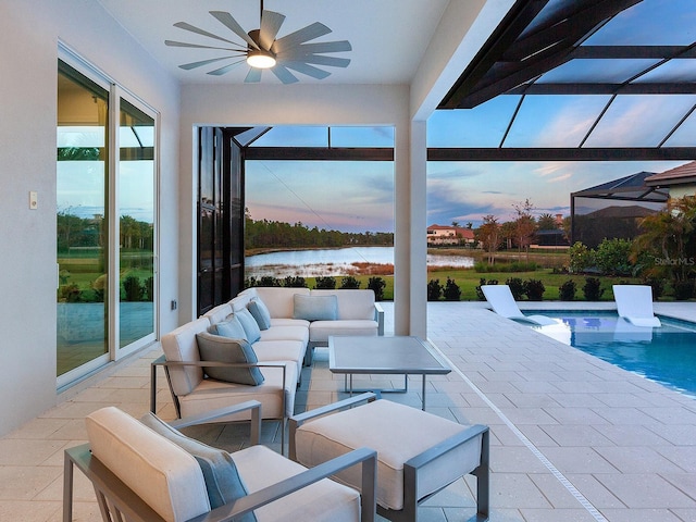 patio terrace at dusk with glass enclosure, ceiling fan, a water view, and an outdoor living space