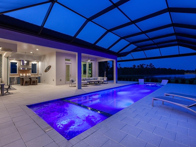 pool at night with ceiling fan, a patio area, an outdoor living space, and glass enclosure