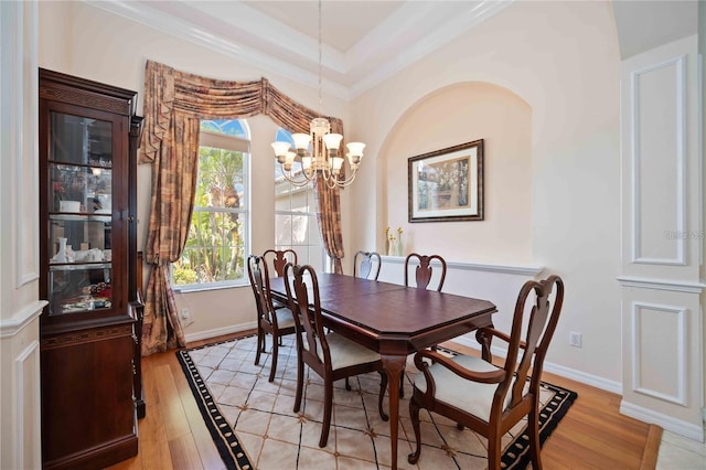 dining area featuring a raised ceiling, a notable chandelier, ornamental molding, and light hardwood / wood-style flooring