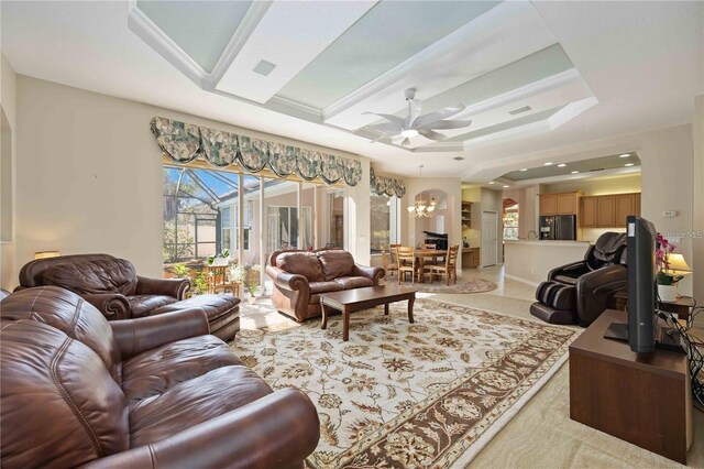 living room featuring ceiling fan with notable chandelier, crown molding, and a raised ceiling