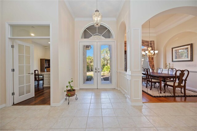 foyer with french doors, light tile patterned flooring, a chandelier, and ornamental molding