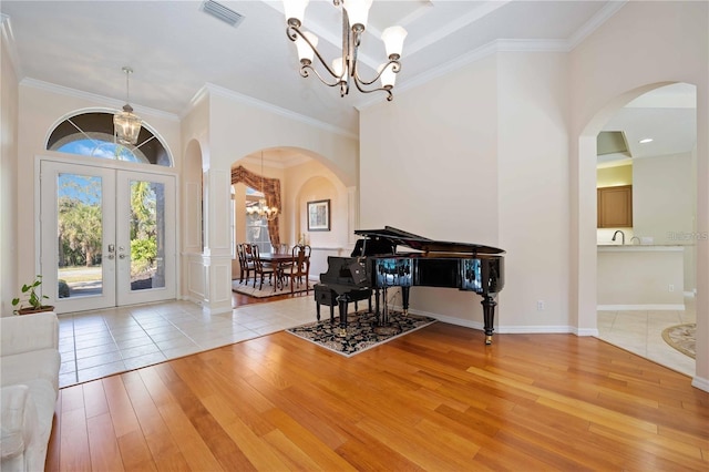 foyer entrance featuring light wood-type flooring, an inviting chandelier, ornamental molding, and french doors