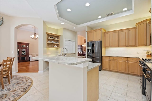 kitchen featuring gas stove, a raised ceiling, a breakfast bar, kitchen peninsula, and stainless steel fridge