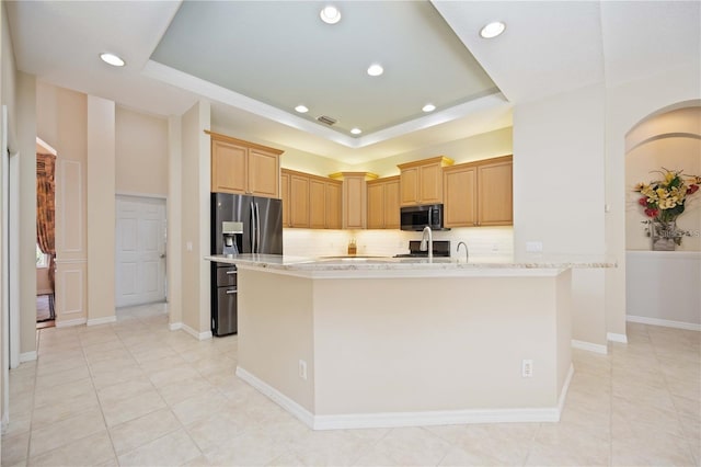 kitchen featuring stainless steel refrigerator with ice dispenser, light brown cabinets, a raised ceiling, tasteful backsplash, and light stone countertops