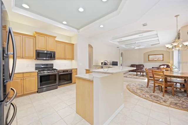 kitchen with light brown cabinets, appliances with stainless steel finishes, a raised ceiling, and light stone counters