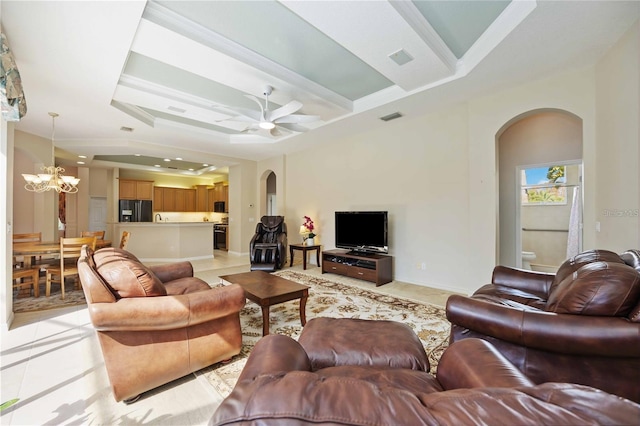 tiled living room featuring a raised ceiling, crown molding, and ceiling fan with notable chandelier