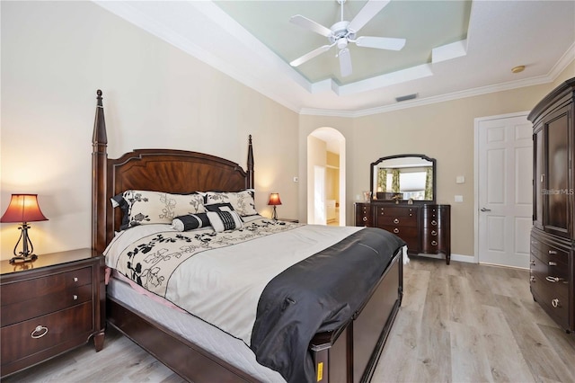 bedroom featuring ceiling fan, a tray ceiling, ornamental molding, and light wood-type flooring