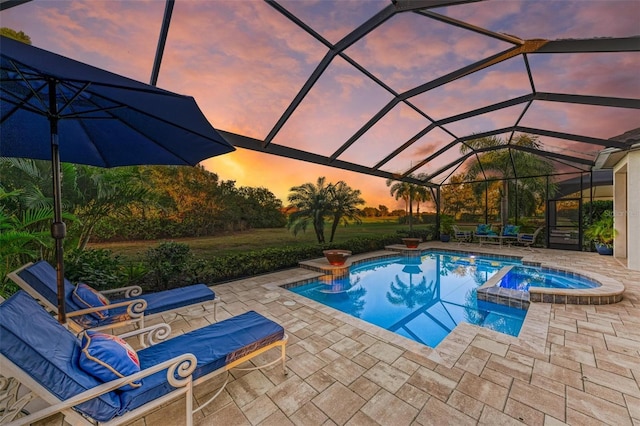 pool at dusk with glass enclosure, a patio area, and an in ground hot tub