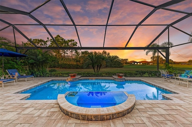 pool at dusk with glass enclosure, a patio area, and an in ground hot tub